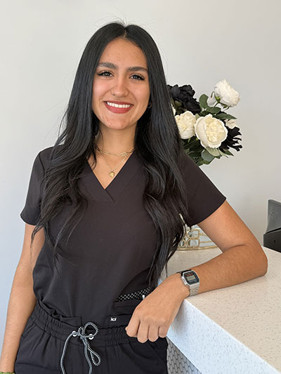 The image features a woman wearing scrubs, standing behind a counter with a white tabletop, smiling at the camera.