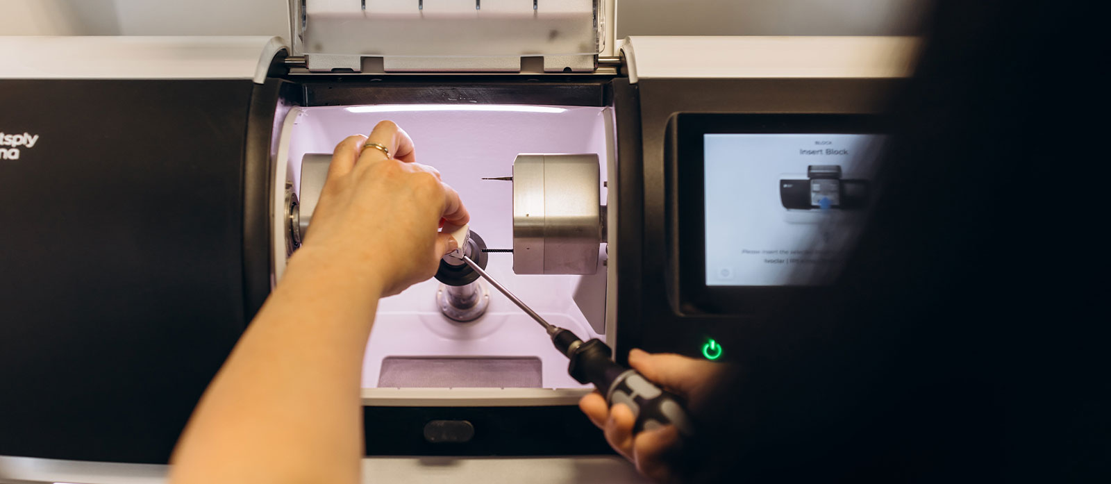The image shows a person operating a 3D printer, with the machine s print bed visible and an object being printed.
