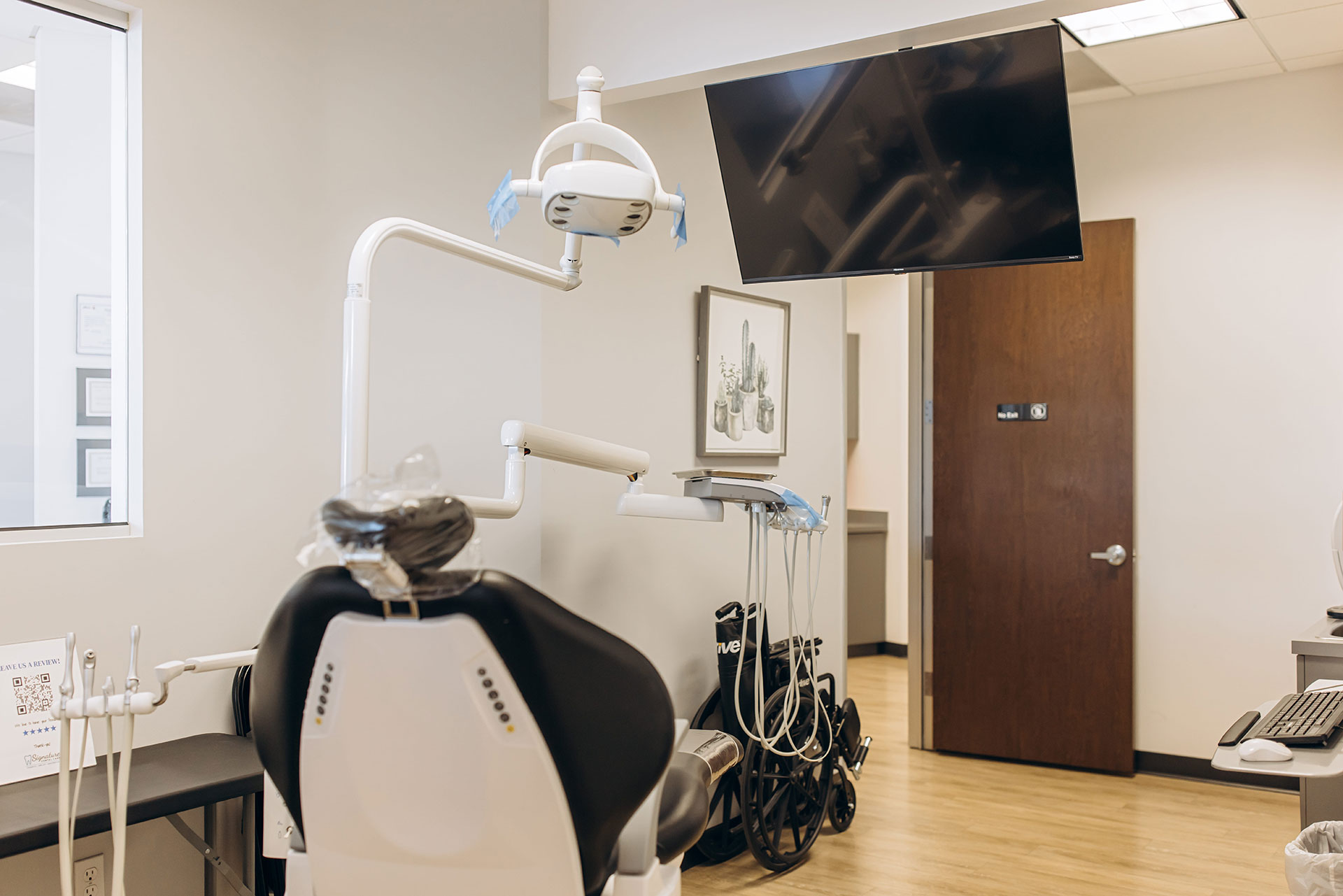 The image shows a dental office interior with various equipment and tools typically found in such a setting, including a dentist s chair, examination table, and dental machines, along with a large window allowing natural light into the room.