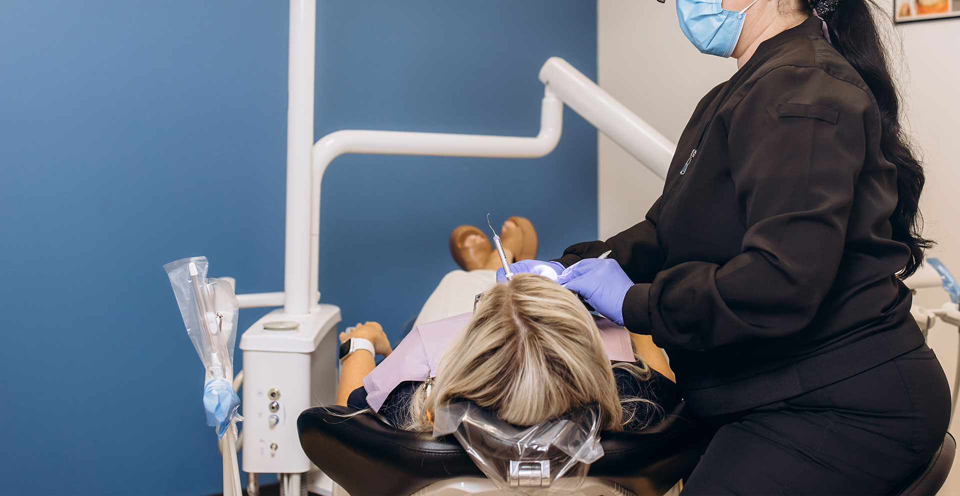 A dental hygienist performing oral care on a patient in a dental chair.