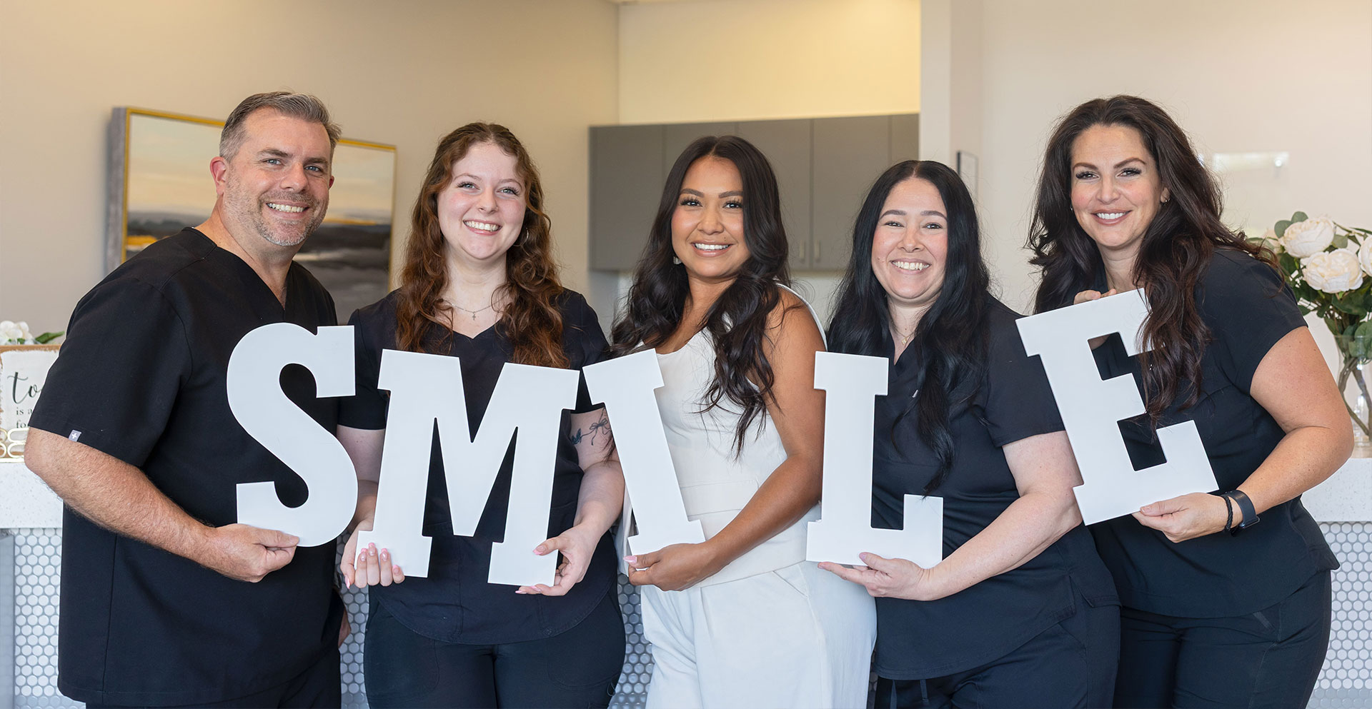 A group of people, including a woman holding a large letter  S  with a smiley face, posing together for a photo.