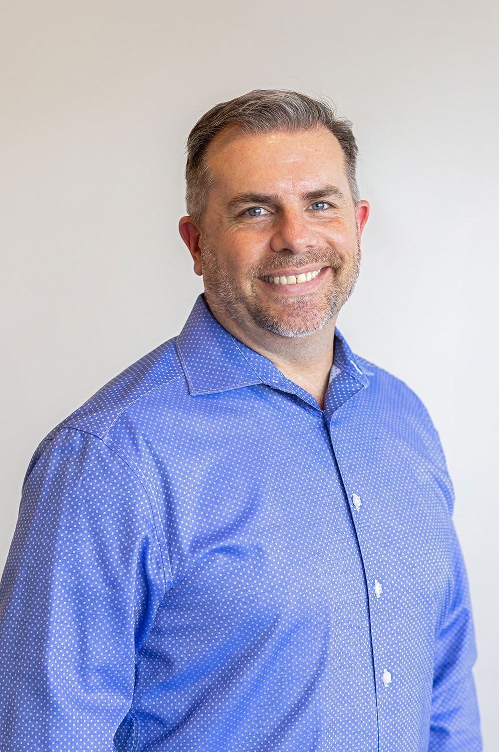 The image shows a man wearing a blue shirt standing against a white background.