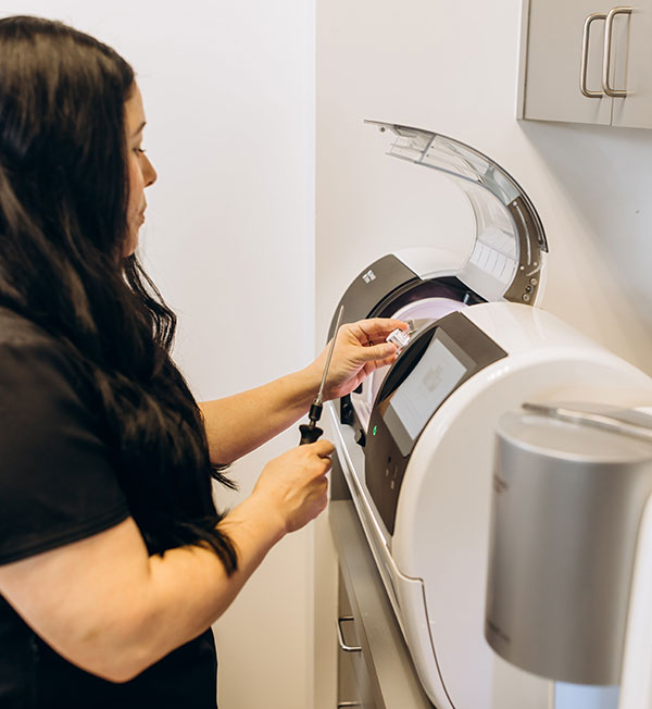 The image shows a woman standing next to an automated kiosk with a receipt printer, interacting with the machine by inserting a card into it.
