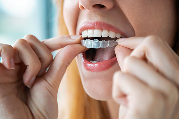 A woman is seen brushing her teeth with an electric toothbrush, wearing lipstick, and holding a toothpaste tube.