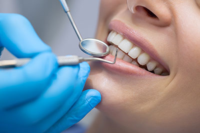A person receiving dental treatment with a dental hygienist using tools to clean their teeth.