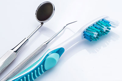 The image shows a collection of dental tools including toothbrushes with blue bristles, a metal dental mirror, and other dental instruments arranged on a white surface.