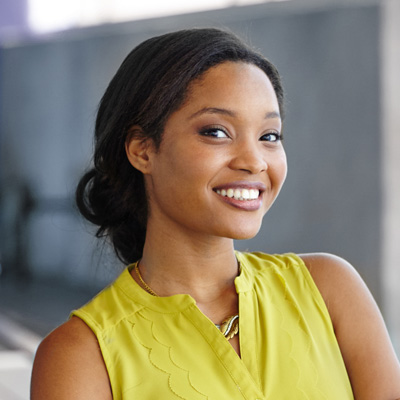 A young woman with short hair, wearing a yellow top and smiling, poses for a portrait.