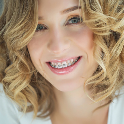 A smiling woman with straight teeth, wearing braces, poses for a portrait with her hair styled in loose waves.