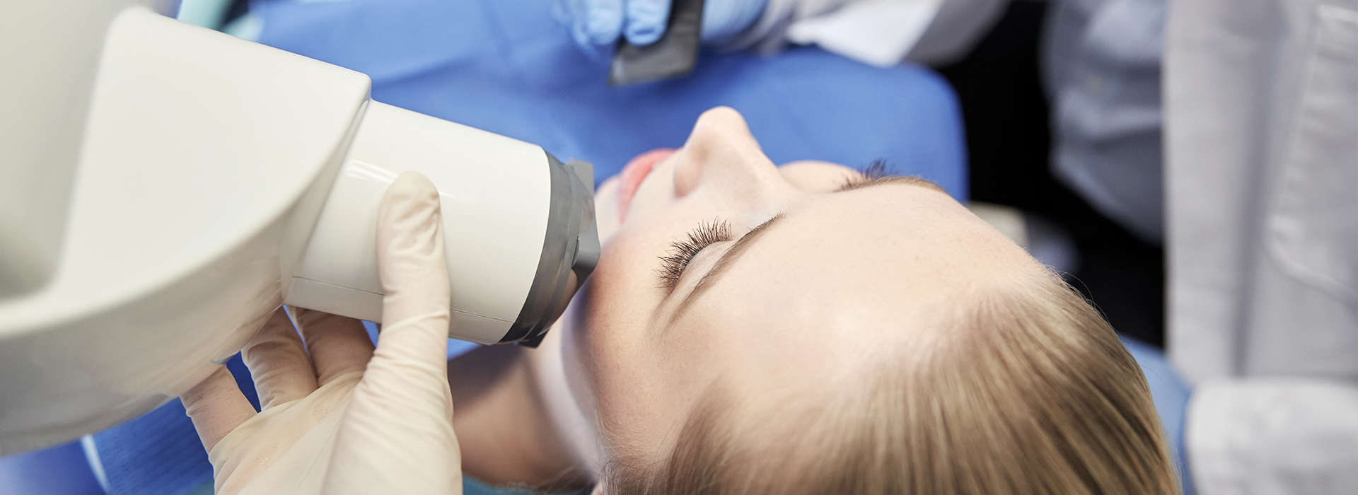 A woman receiving a medical procedure with a microscope, likely at a dental clinic, under the supervision of a professional.