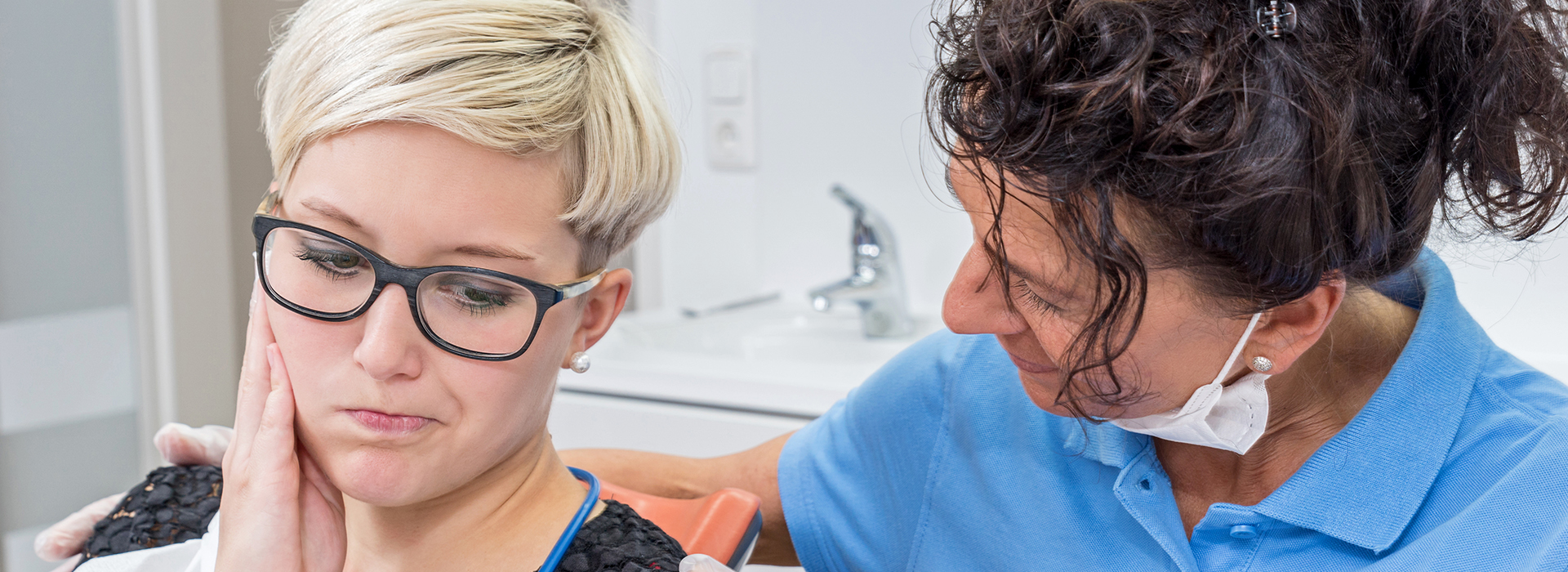 The image shows a dental professional assisting a patient with a dental procedure, likely an examination or cleaning, in a dental office setting.