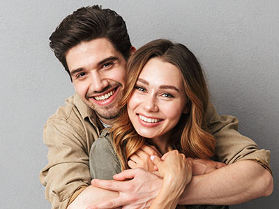 A young couple embracing closely, smiling at each other against a neutral background.