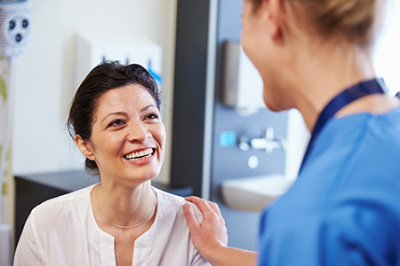 The image shows a woman with a smile, standing next to a man wearing a stethoscope, in an indoor setting that appears to be a medical facility.
