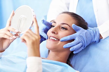 A woman receiving a facial treatment with a magnifying mirror held over her face by a professional.