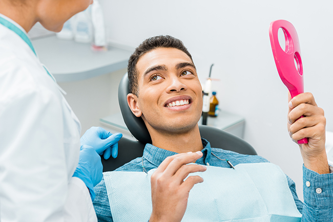 A young man in a dental chair receiving treatment from a dentist, with an oral hygiene device being used on his teeth.