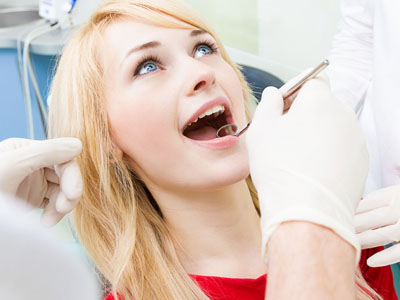The image depicts a woman seated in a dental chair receiving dental care, with a dentist performing a procedure on her teeth while she is undergoing sedation.