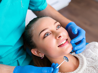 A woman receiving dental care with a dentist assisting her while smiling.
