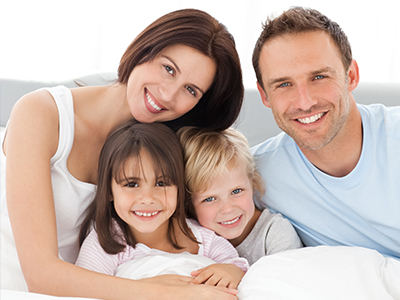 A family of four people sitting together on a bed with a smiling expression.