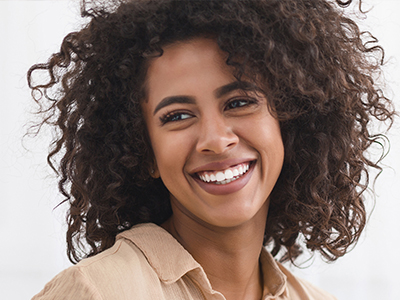 A woman with curly hair smiling at the camera, wearing a light-colored top and earrings, against a white background.